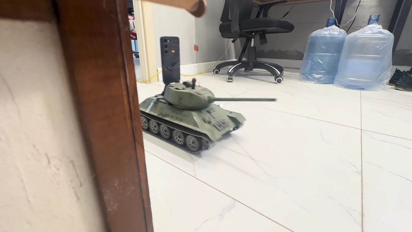 Physical 1:16 tank moving through a miniature arena between buildings and obstacles